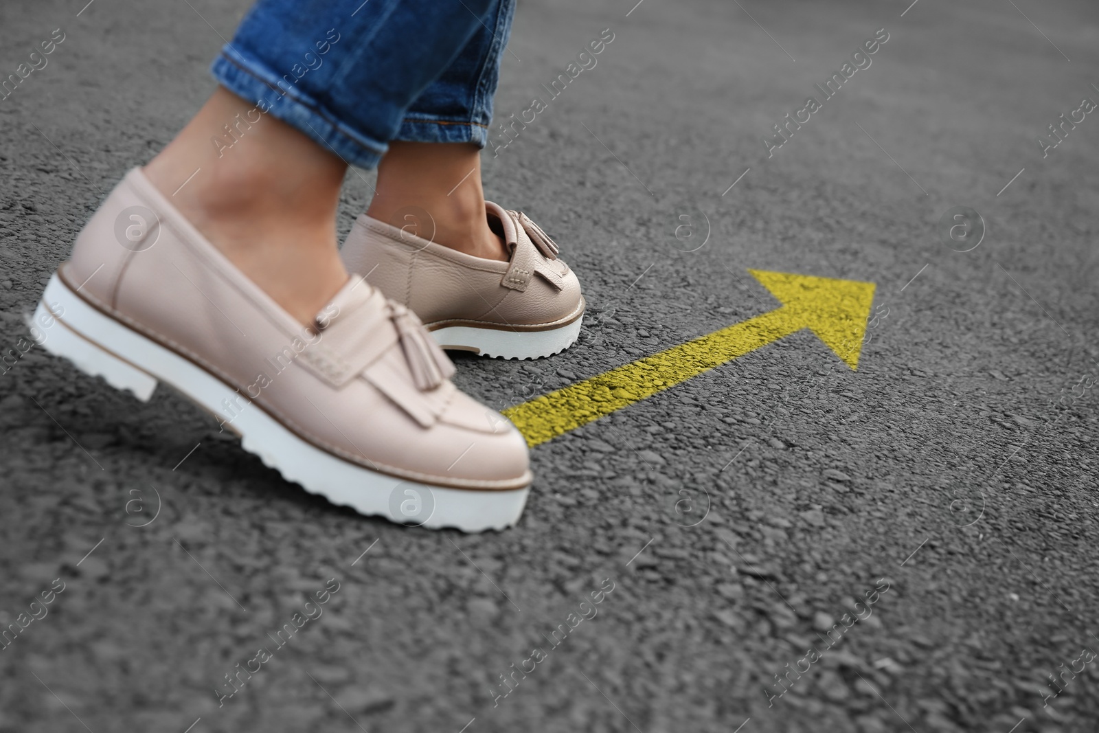 Image of Woman walking on asphalt road with yellow arrow, closeup. Concepts of choice, decision, moving forward