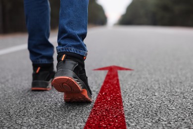 Image of Man walking on asphalt road with red arrow, closeup. Concepts of choice, decision, moving forward