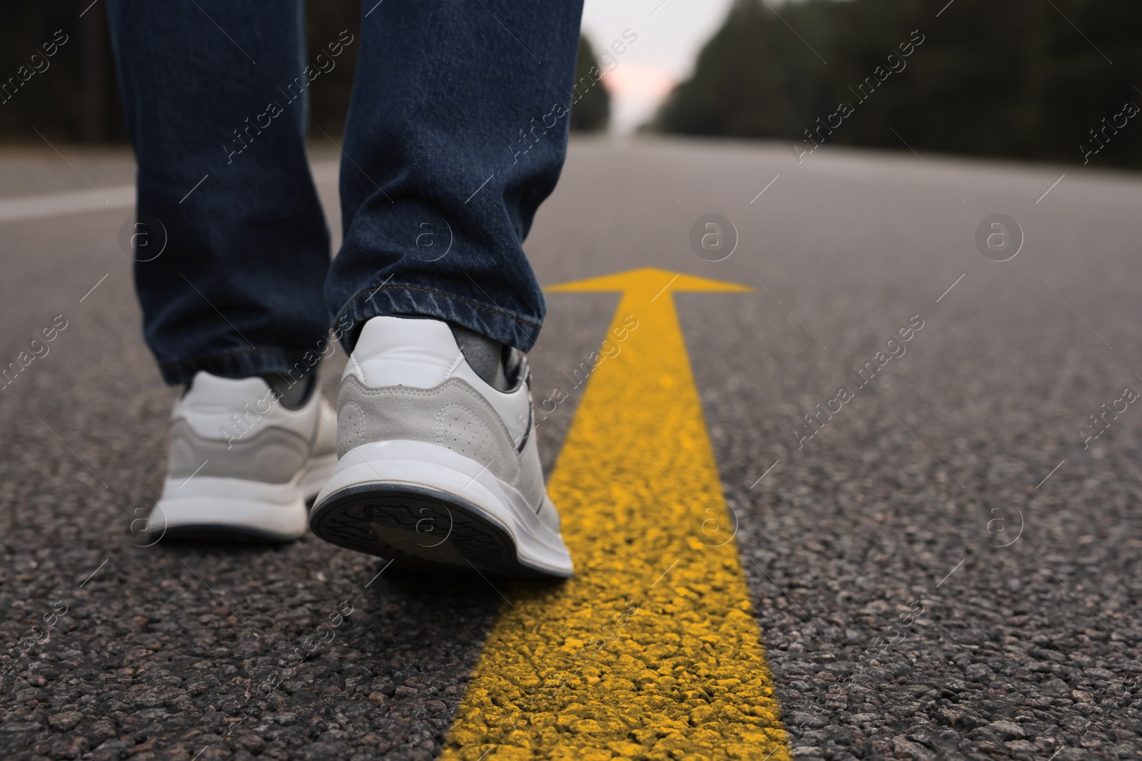 Image of Man walking on asphalt road with yellow arrow, closeup. Concepts of choice, decision, moving forward