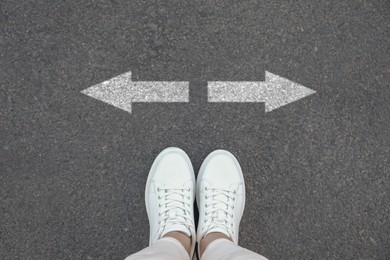 Image of Woman standing near white arrows on asphalt road, closeup. Concepts of choice, decision, different way, alternative