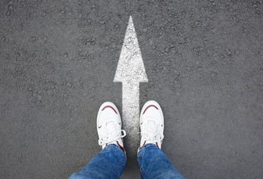 Image of Man standing near white arrow on asphalt road, closeup. Concepts of choice, decision, moving forward