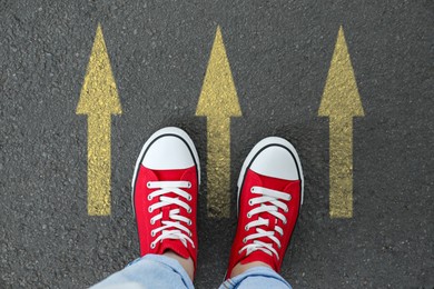 Image of Woman standing near yellow arrows on asphalt road, closeup. Concepts of choice, decision, moving forward