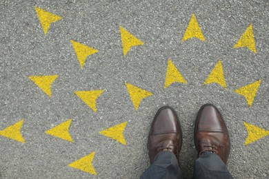 Image of Man standing near yellow arrows on asphalt road, closeup. Concepts of choice, decision, different way, alternative