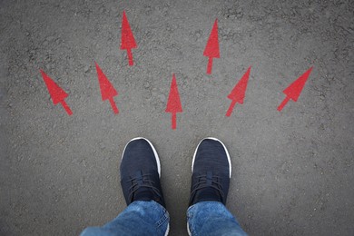 Image of Man standing near red arrows on asphalt road, closeup. Concepts of choice, decision, different way, alternative