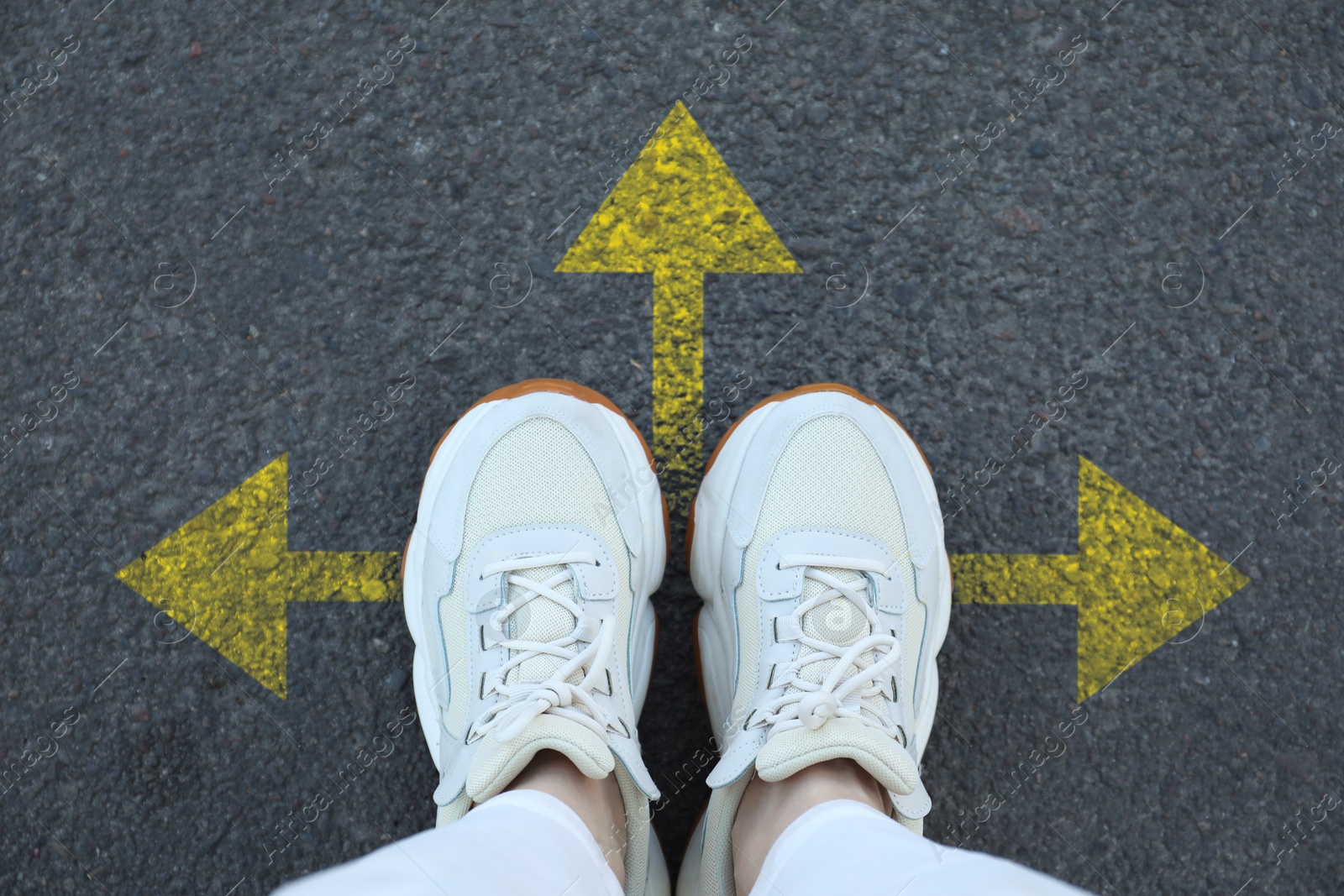 Image of Woman standing near yellow arrows on asphalt road, closeup. Concepts of choice, decision, different way, alternative