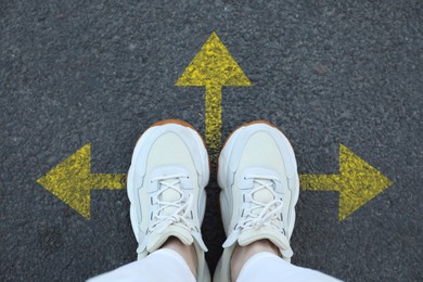 Image of Woman standing near yellow arrows on asphalt road, closeup. Concepts of choice, decision, different way, alternative