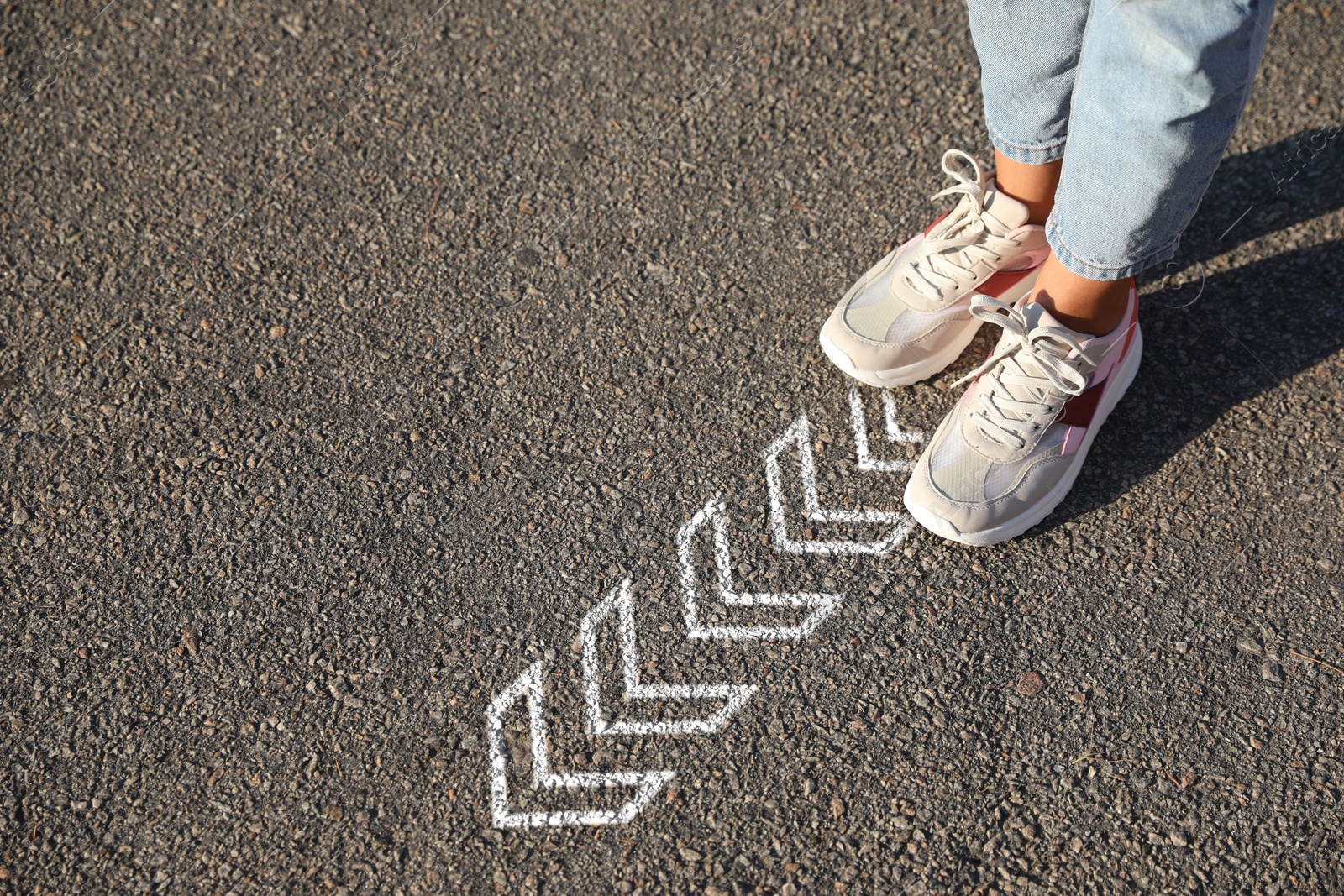 Image of Woman standing near white arrows on asphalt road, closeup. Concepts of choice, decision, moving forward