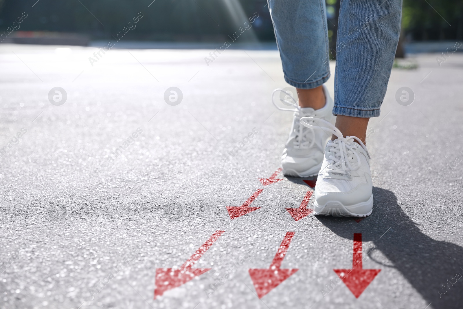 Image of Woman walking on asphalt road with red arrows, closeup. Concepts of choice, decision, moving forward