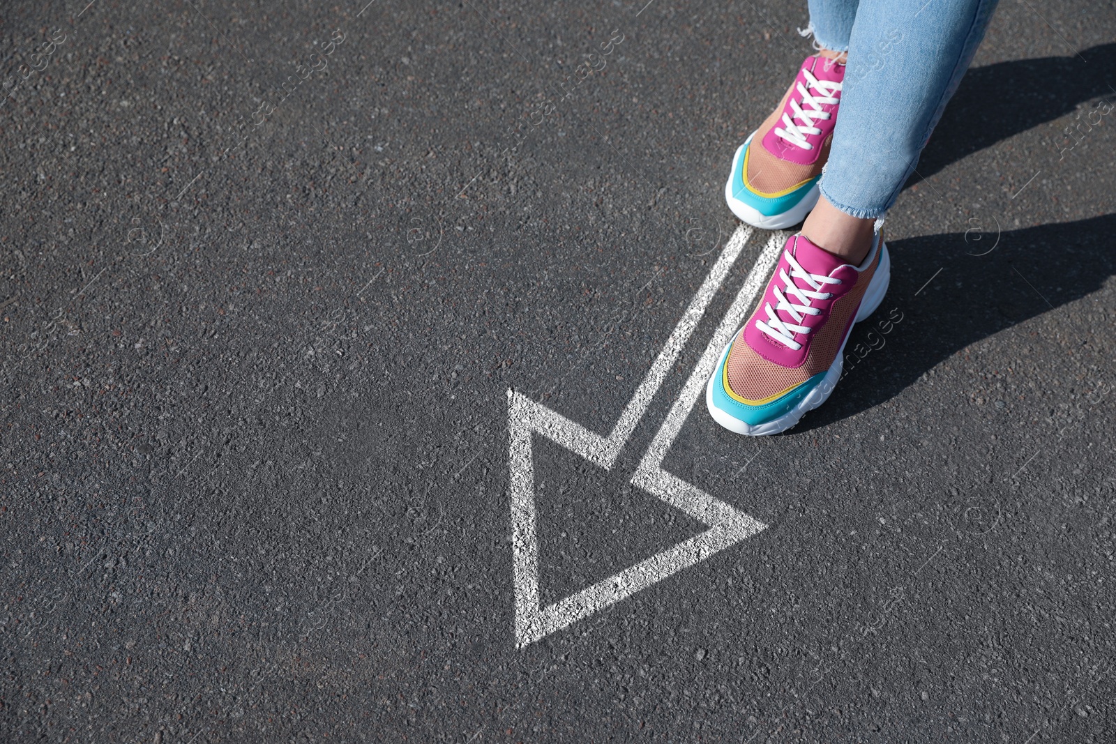 Image of Woman walking on asphalt road with white arrow, closeup. Concepts of choice, decision, moving forward