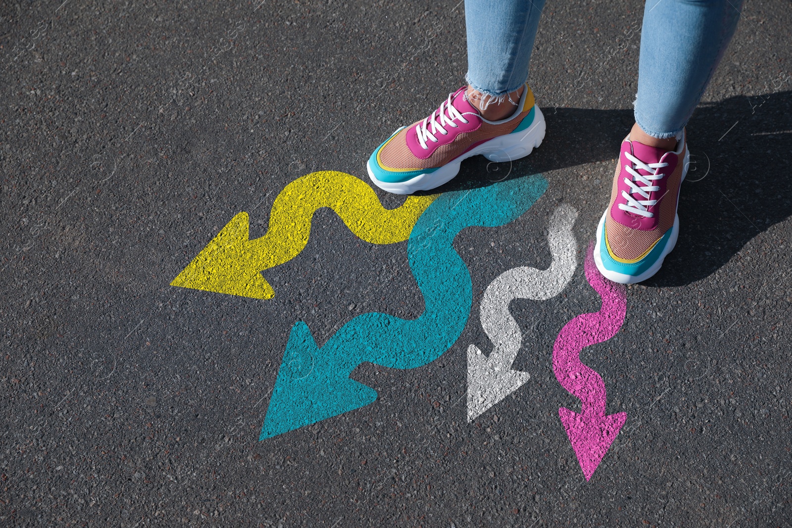 Image of Woman standing near colorful arrows on asphalt road, closeup. Concepts of choice, decision, different way, alternative