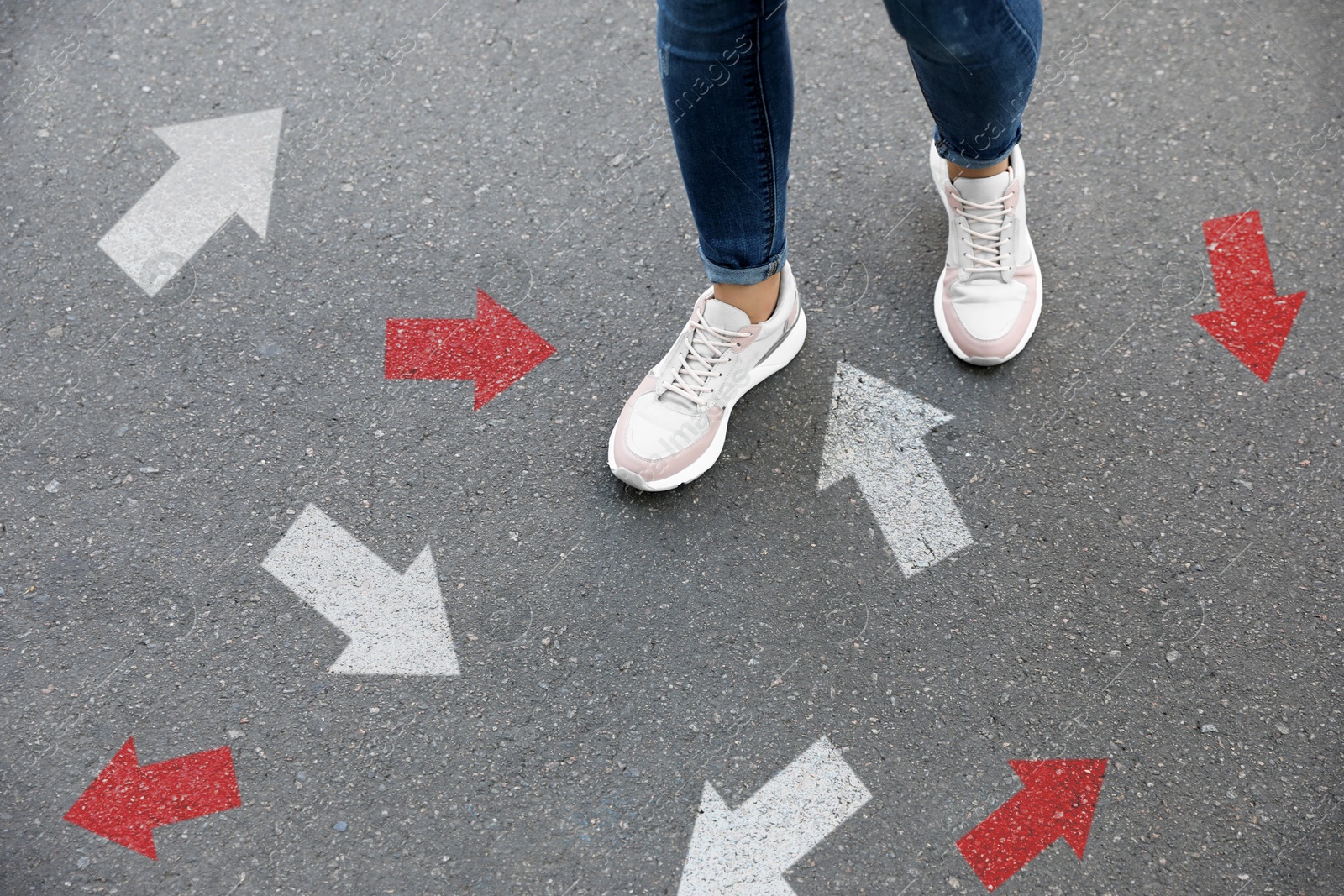 Image of Woman walking on asphalt road with red and white arrows pointing in different directions, closeup. Concepts of choice, decision, alternative way