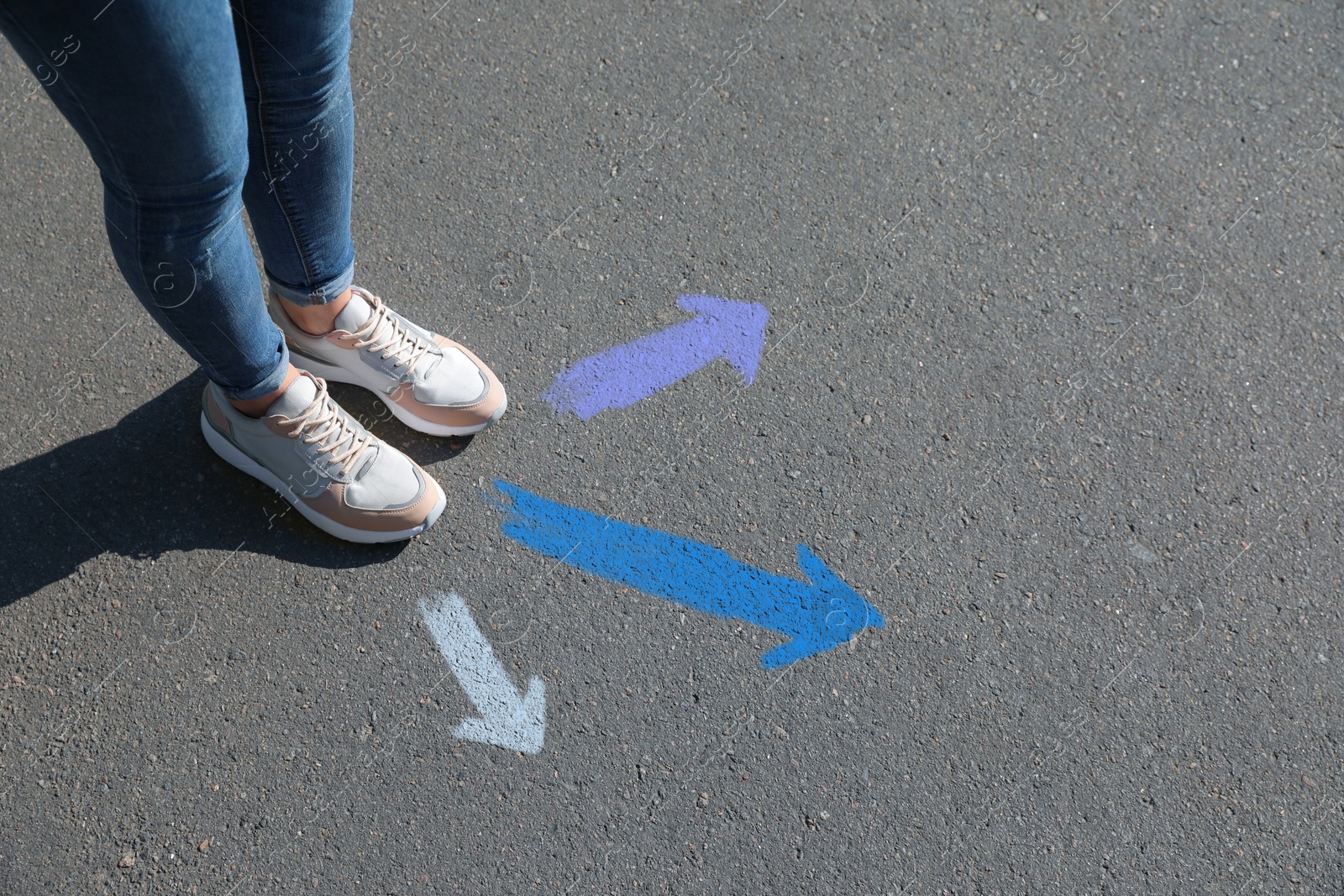 Image of Woman standing near colorful arrows on asphalt road, closeup. Concepts of choice, decision, different way, alternative