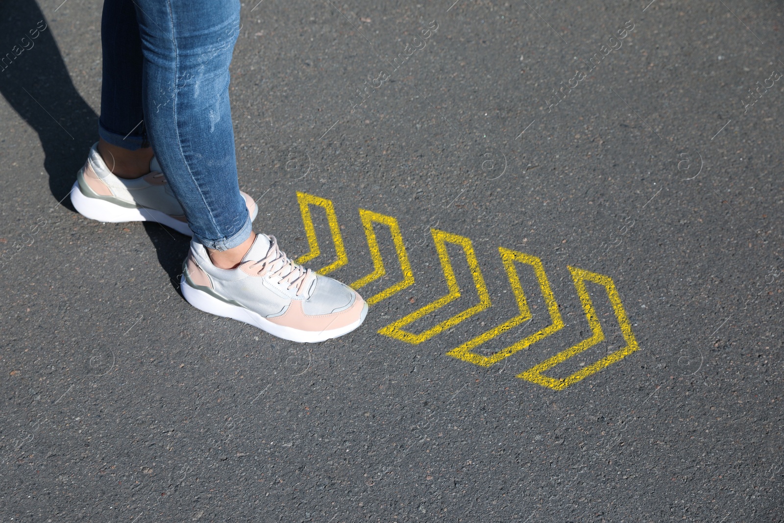 Image of Woman walking on asphalt road with yellow arrows, closeup. Concepts of choice, decision, moving forward