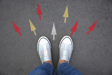 Image of Woman standing near colorful arrows on asphalt road, closeup. Concepts of choice, decision, different way, alternative