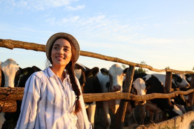 Photo of Young woman standing near cow pen on farm. Animal husbandry