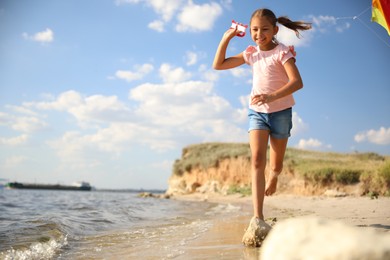 Photo of Cute little child with kite running on beach near sea. Spending time in nature