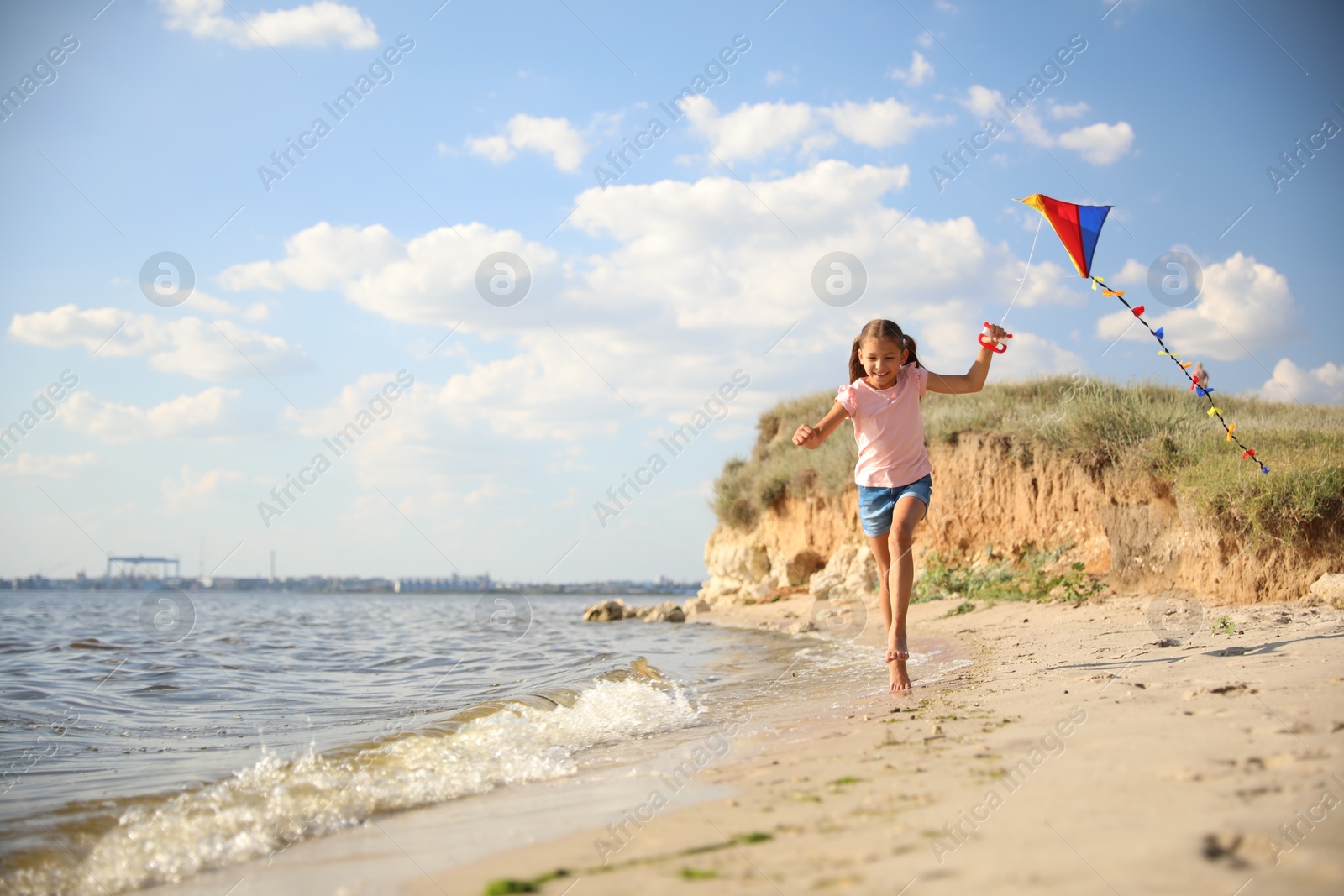 Photo of Cute little child with kite running on beach near sea. Spending time in nature