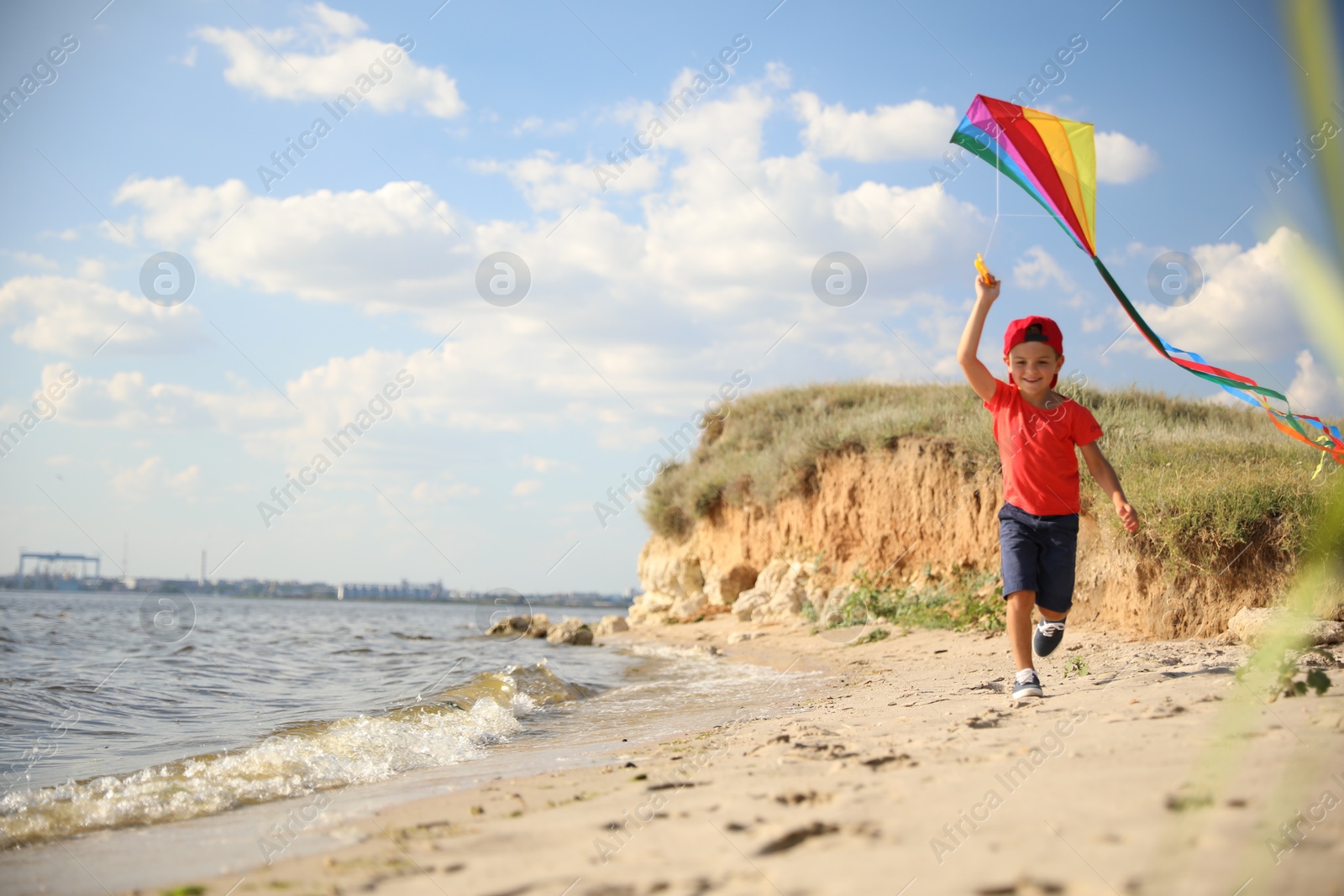 Photo of Cute little child with kite running on beach near sea. Spending time in nature