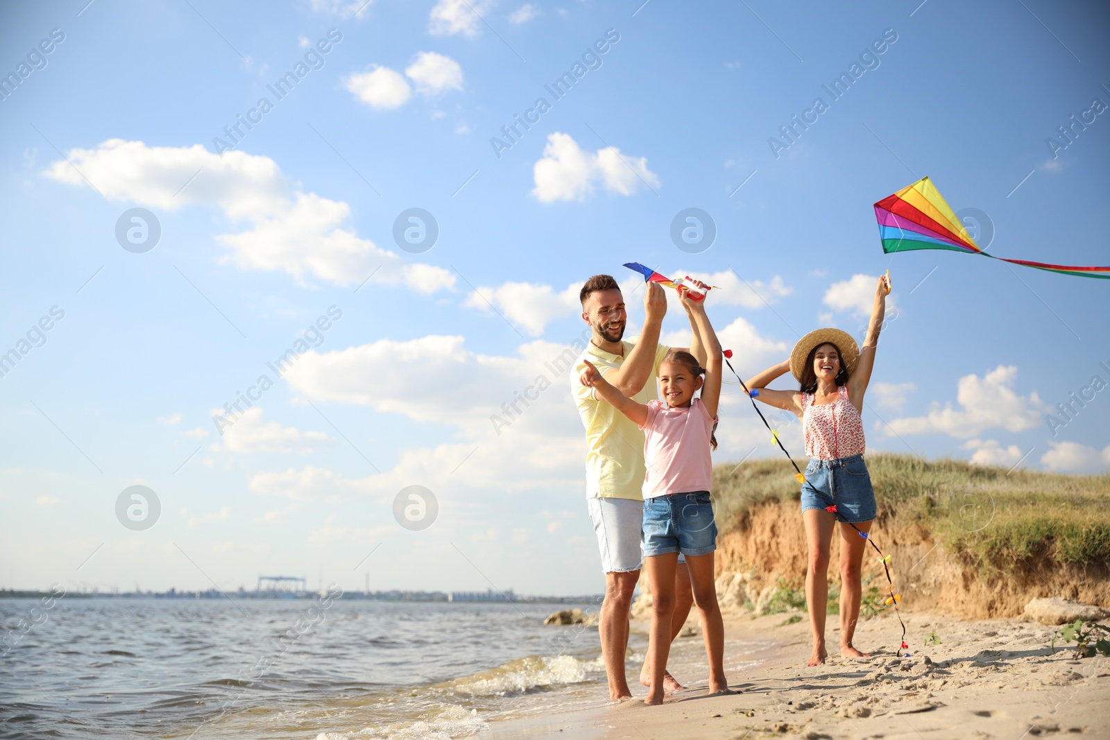 Photo of Happy parents and their child playing with kites on beach near sea. Spending time in nature