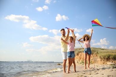 Photo of Happy parents and their child playing with kites on beach near sea. Spending time in nature