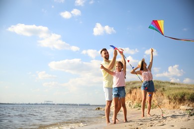 Photo of Happy parents and their child playing with kites on beach near sea. Spending time in nature