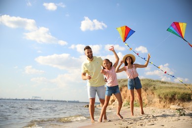 Photo of Happy parents and their child playing with kites on beach near sea. Spending time in nature