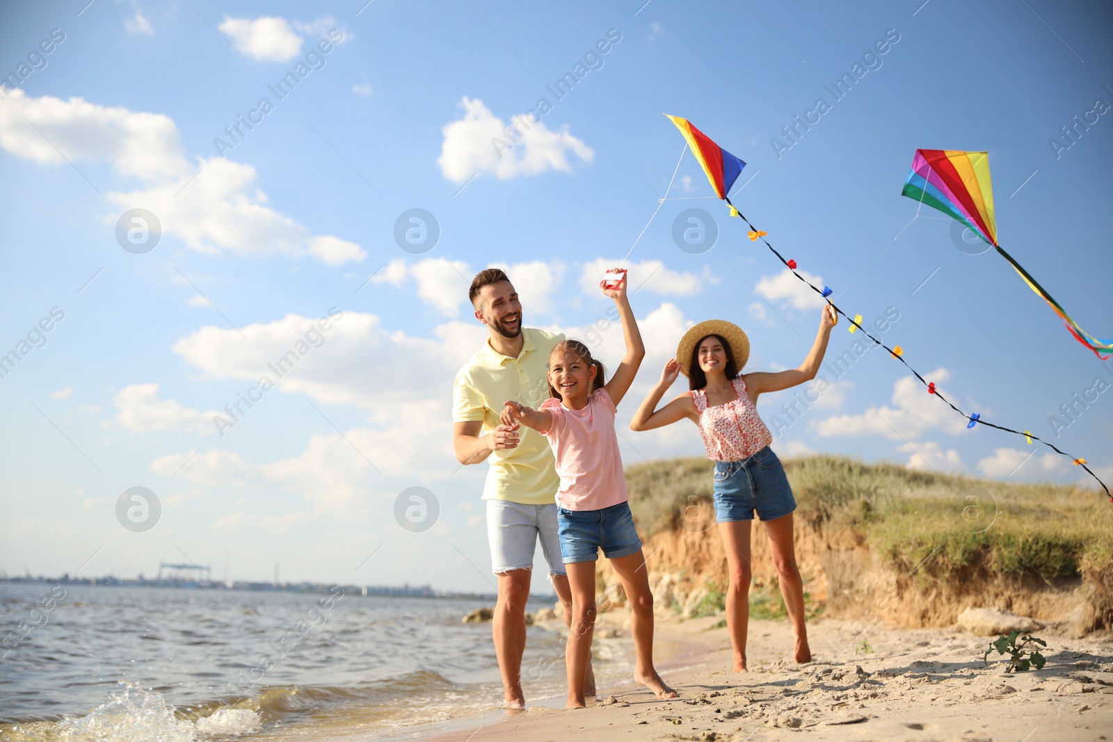 Photo of Happy parents and their child playing with kites on beach near sea. Spending time in nature