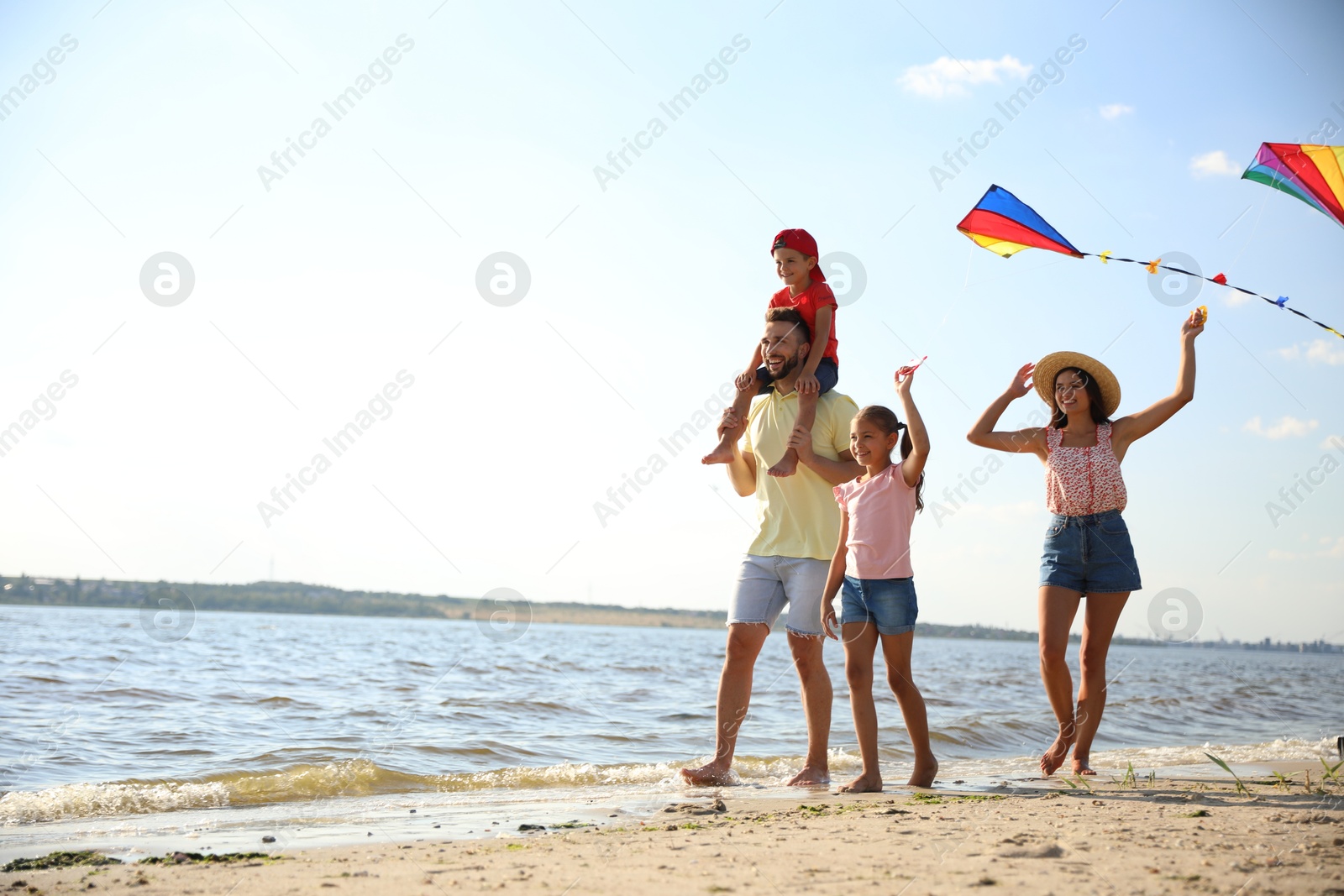 Photo of Happy parents and their children playing with kites on beach near sea. Spending time in nature