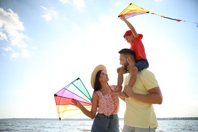 Photo of Happy parents and their child playing with kites near sea. Spending time in nature