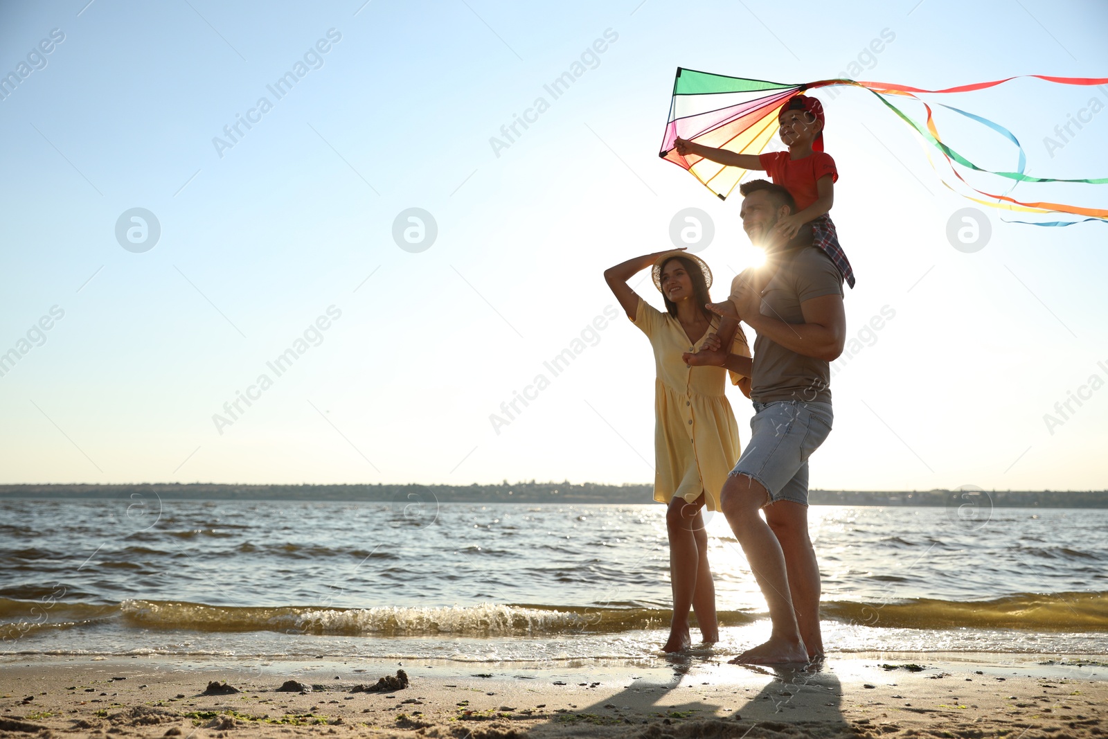 Photo of Happy parents and their child playing with kite on beach near sea. Spending time in nature