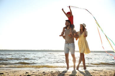 Photo of Happy parents and their child playing with kite on beach near sea. Spending time in nature