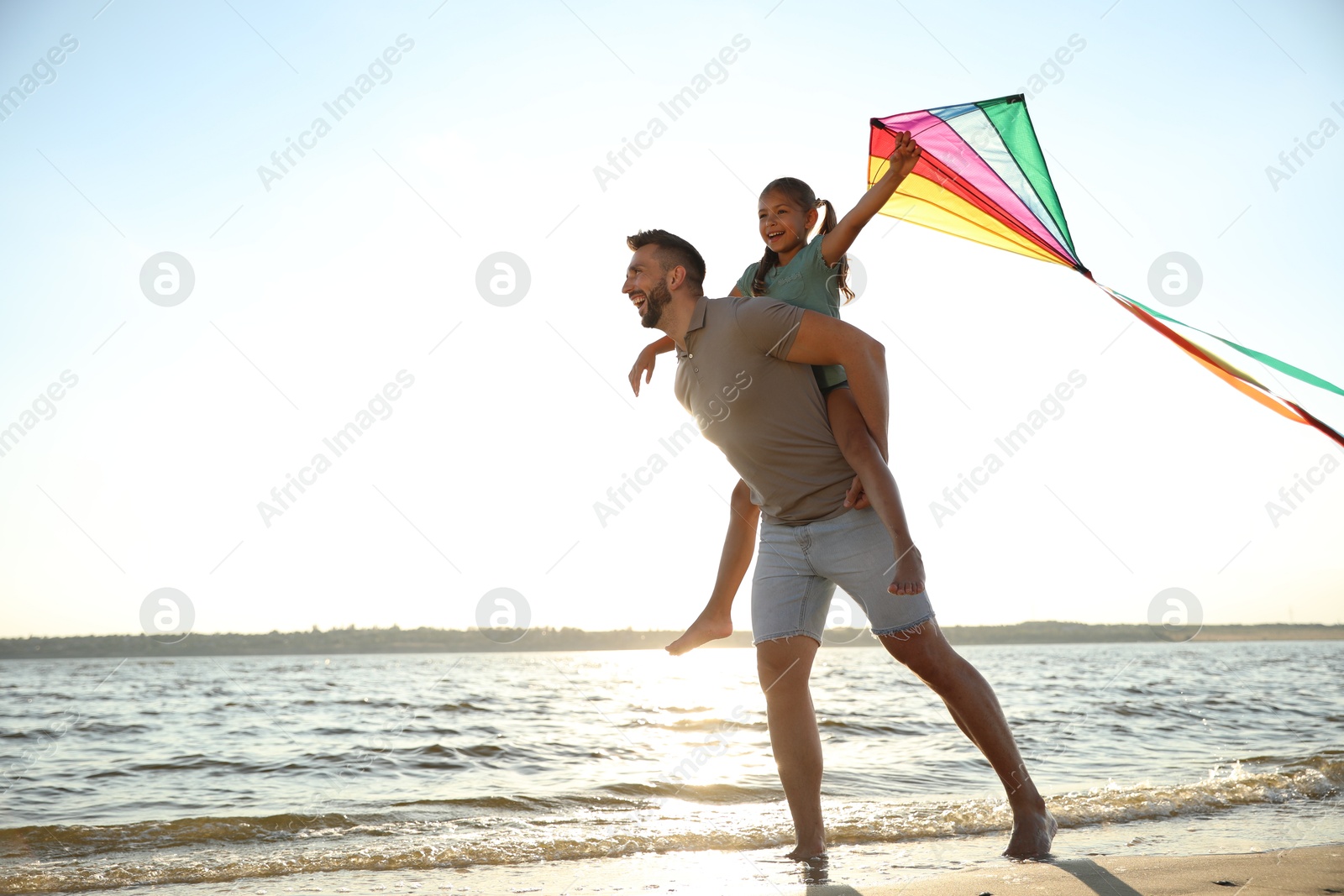 Photo of Happy father and his child playing with kite on beach near sea. Spending time in nature