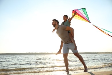 Photo of Happy father and his child playing with kite on beach near sea. Spending time in nature