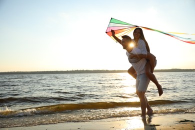 Photo of Happy couple playing with kite on beach near sea at sunset. Spending time in nature