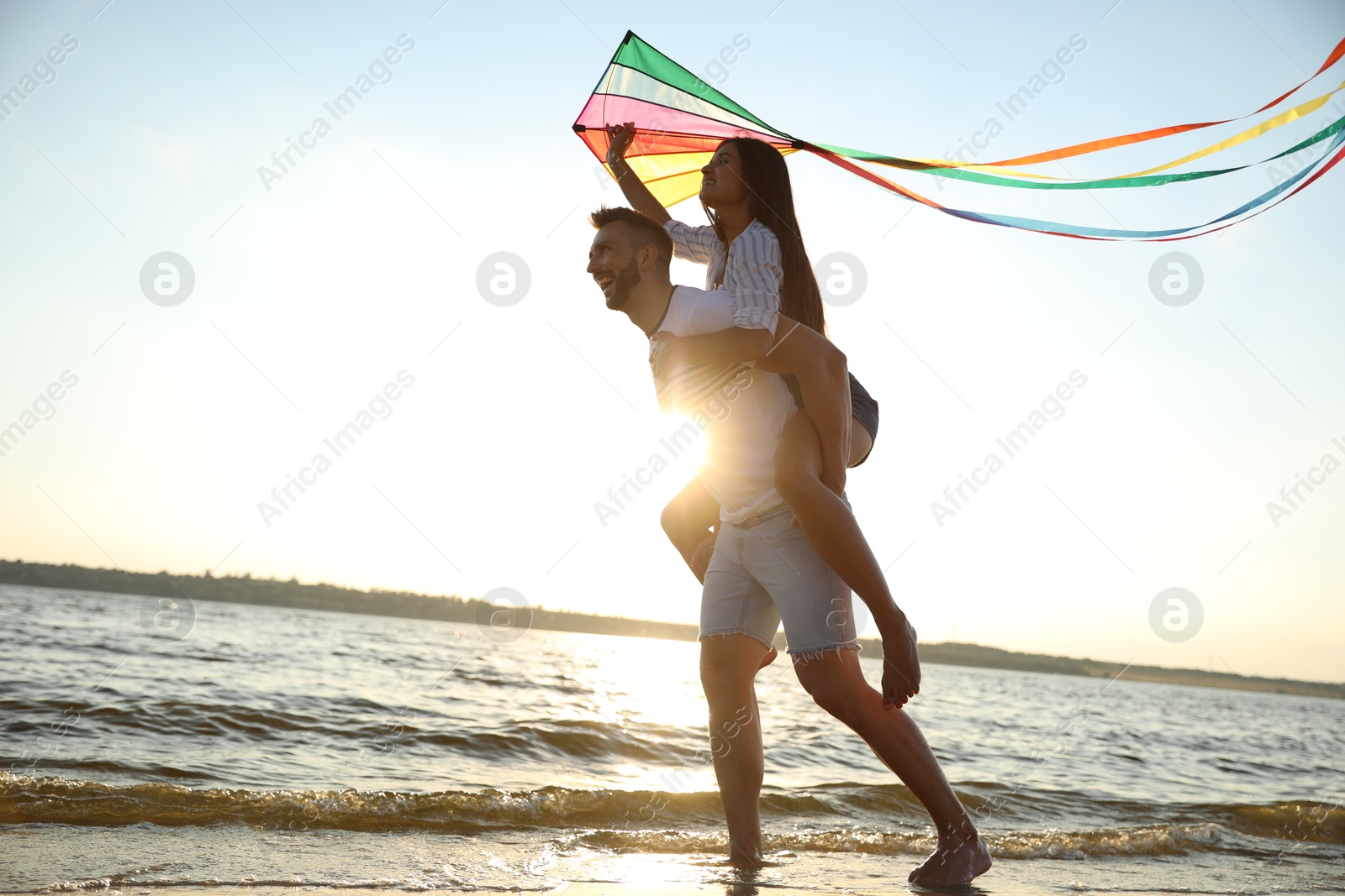 Photo of Happy couple playing with kite on beach near sea at sunset. Spending time in nature