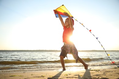 Photo of Cute little child with kite running on beach near sea at sunset. Spending time in nature