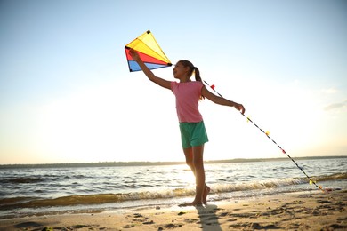 Photo of Cute little child playing with kite on beach near sea at sunset. Spending time in nature