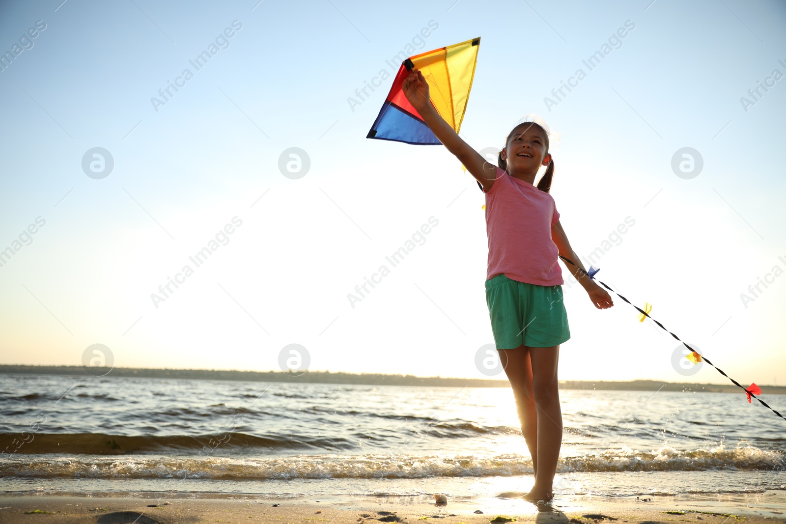 Photo of Cute little child playing with kite on beach near sea at sunset. Spending time in nature