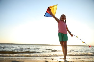 Photo of Cute little child playing with kite on beach near sea at sunset. Spending time in nature