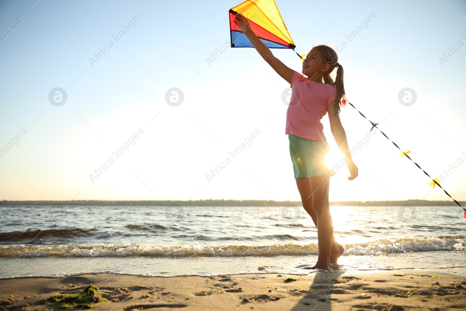 Photo of Cute little child playing with kite on beach near sea at sunset. Spending time in nature