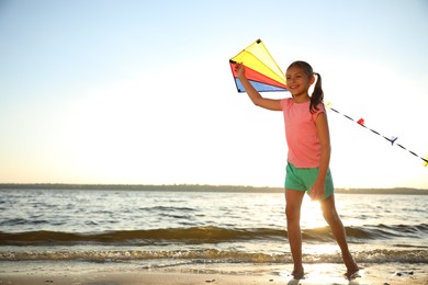 Photo of Cute little child playing with kite on beach near sea at sunset. Spending time in nature