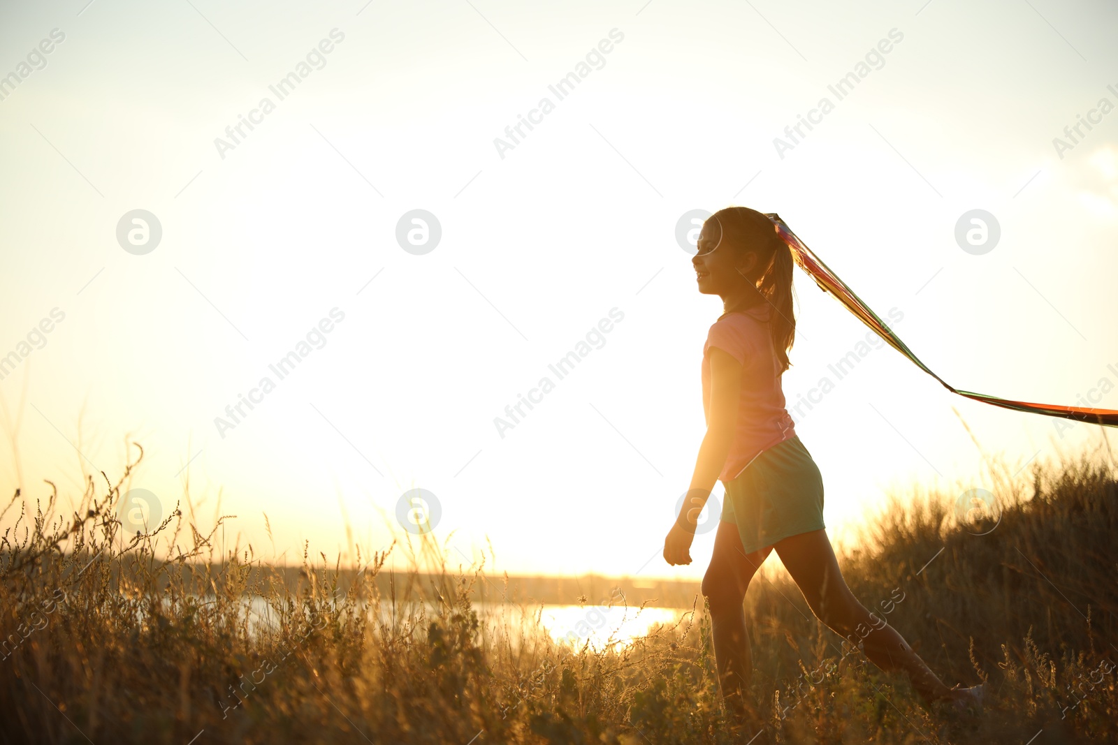 Photo of Cute little child with kite running outdoors at sunset. Spending time in nature