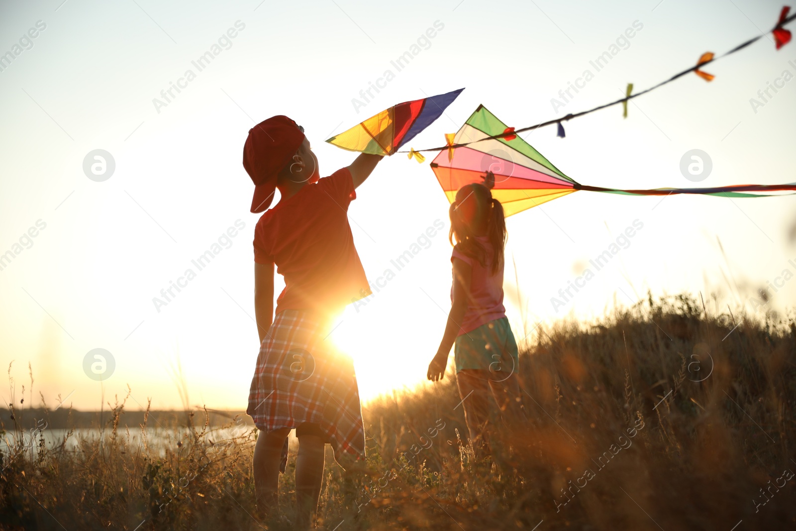 Photo of Little children playing with kites outdoors at sunset. Spending time in nature