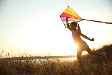 Photo of Cute little child playing with kite outdoors at sunset. Spending time in nature