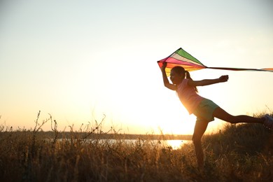 Photo of Cute little child playing with kite outdoors at sunset. Spending time in nature