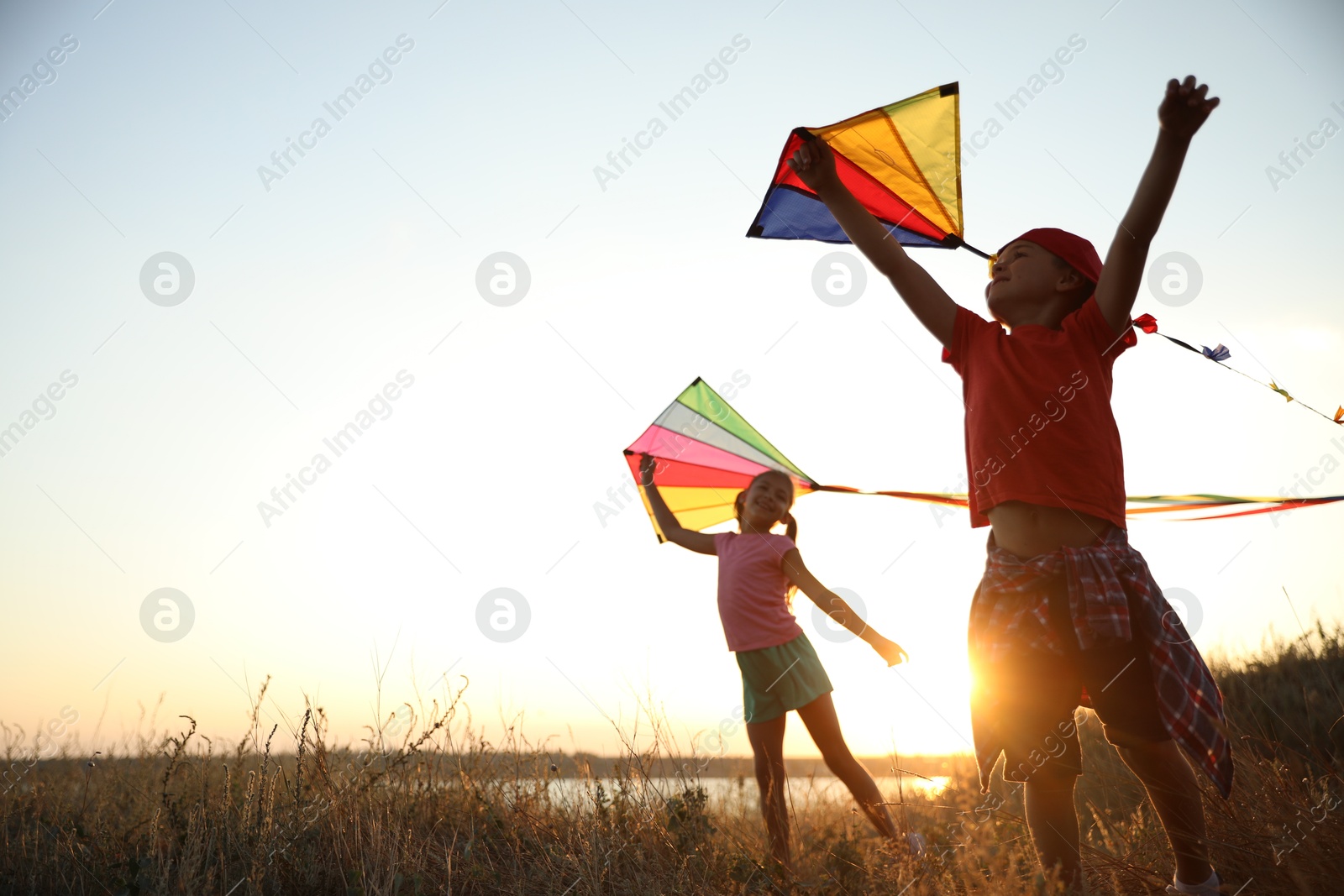 Photo of Cute little children playing with kites outdoors at sunset. Spending time in nature