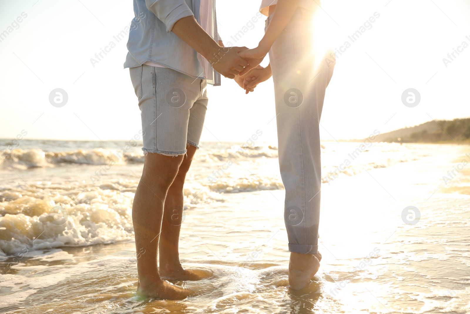 Photo of Couple on sandy beach near sea at sunset, closeup of legs