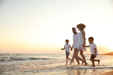 Photo of Happy family running on sandy beach near sea at sunset