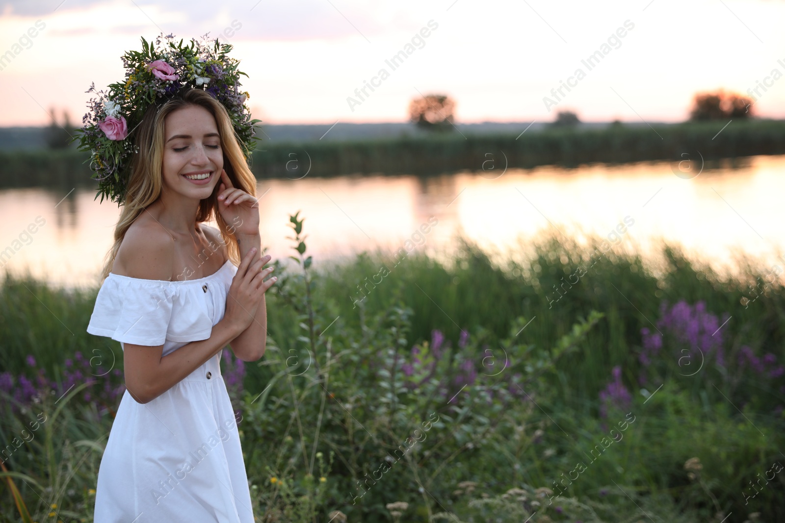 Photo of Young woman wearing wreath made of beautiful flowers outdoors at sunset