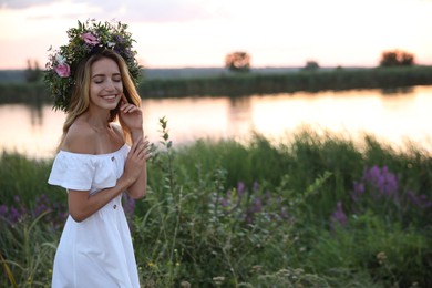 Photo of Young woman wearing wreath made of beautiful flowers outdoors at sunset